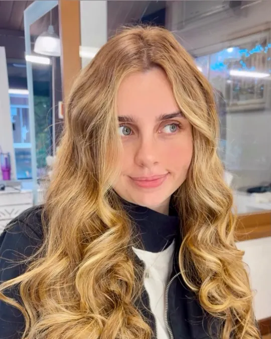 Cliente de cabelo loiro longo com ondas largas, sorrindo, no Le Visage