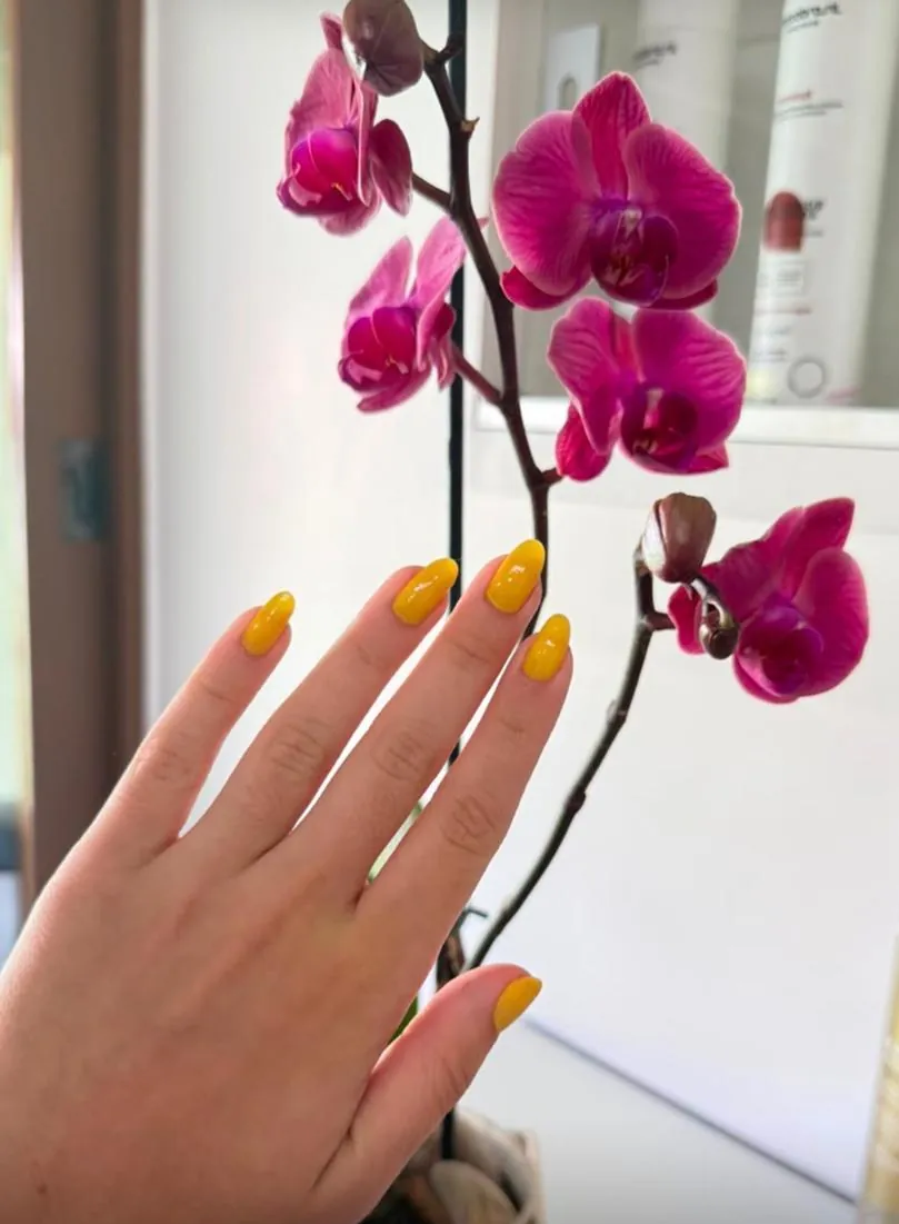 Mão com unhas esmaltadas de amarelo ao lado de uma orquídea